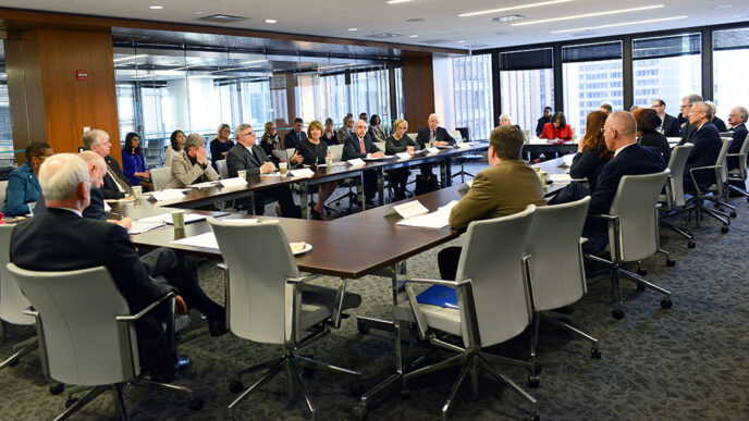 Representatives of 20 colleges meet around a table.
