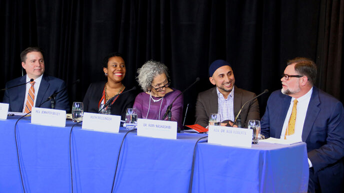 Five people seated behind a table for a panel discussion. The man seated at far right is speaking.