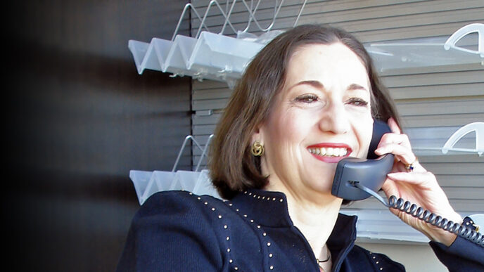 A woman smiles while talking on the phone in an office|A woman smiles while talking on the phone in a wood-paneled office|Three women stand on stage smiling and holding an award plaque.