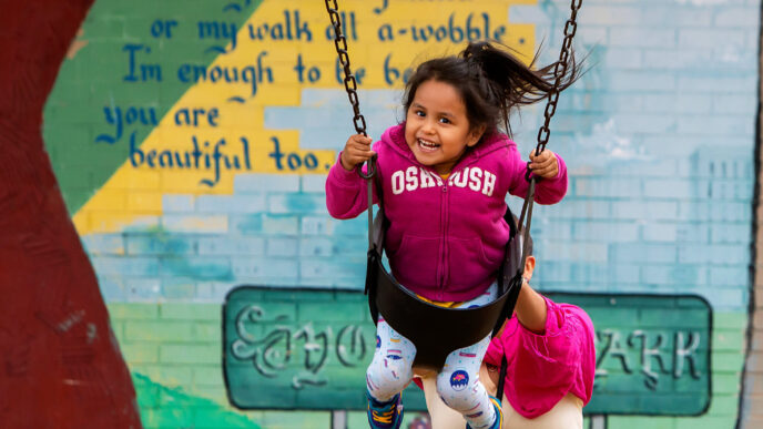 A woman pushing a smiling young girl in a swing at Rogers Park.