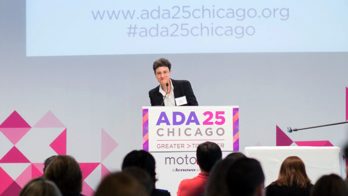 Emily Harris standing on stage at a podium with a sign that reads ADA 25 Chicago – Greater Together|.