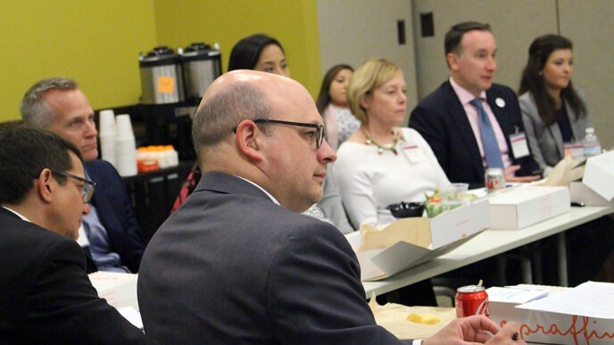 A group of men and women sit around a large table with boxed lunches