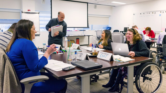 Four people seated in chars and wheelchairs around a table in a conference room