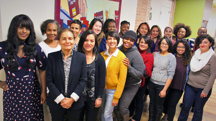 Nineteen women standing in a group indoors.