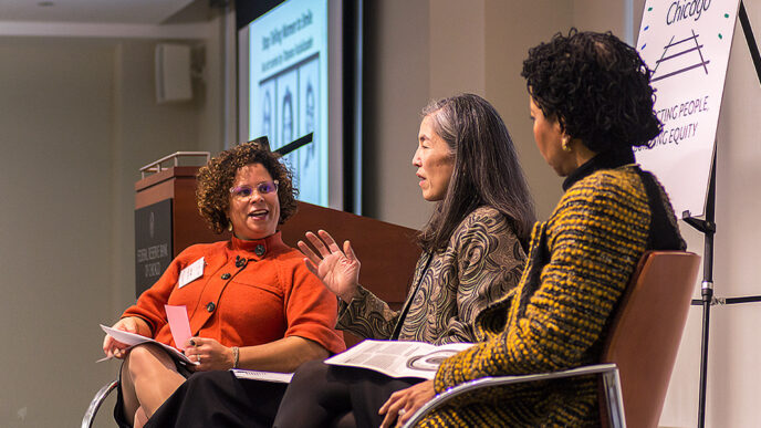 Three women sit in chairs in a stage
