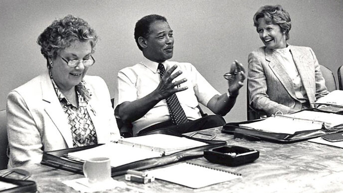 Black & white archival photo of a meeting at the Trust’s offices. At a conference table covered with binders and papers