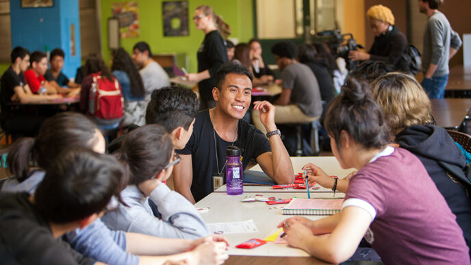 A smiling young man seated around a table with a group of high school students