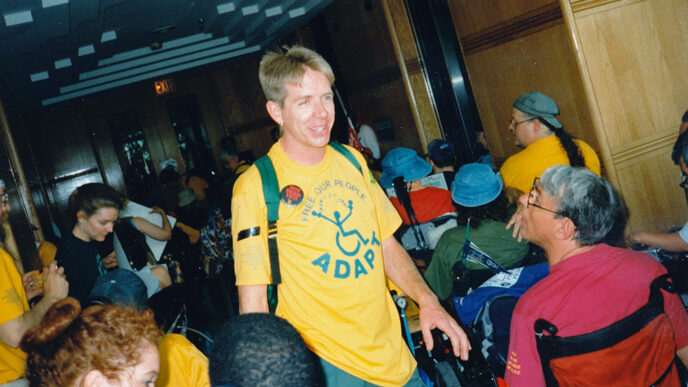 A man wearing a t-shirt that says ADAPT amid a group of people using wheelchairs|Vintage photo of protestors shouting and holding signs