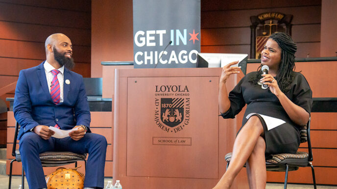Two people sit in chairs at the front of a lecture hall.