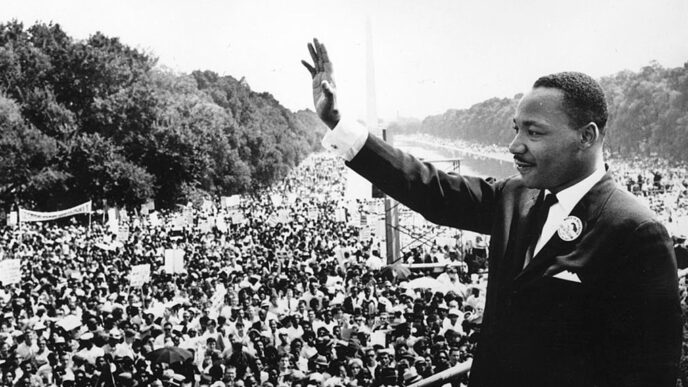 Rev. Dr. Martin Luther King Jr. stands on a podium overlooking the crowd at the 1963 March on Washington|Four men.