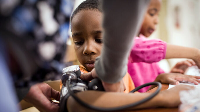 A young boy watches the hands of a nurse fastening a blood pressure cuff around his arm.