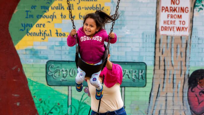 A woman pushing a smiling young girl in a swing at Rogers Park.