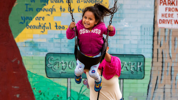 A woman pushing a smiling young girl in a swing at Rogers Park