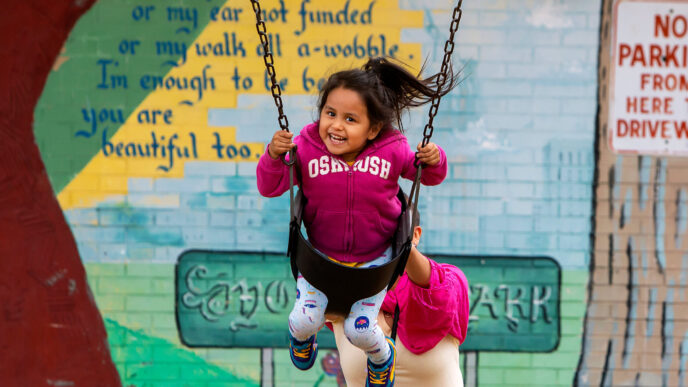 A woman pushing a smiling young girl in a swing at Rogers Park.