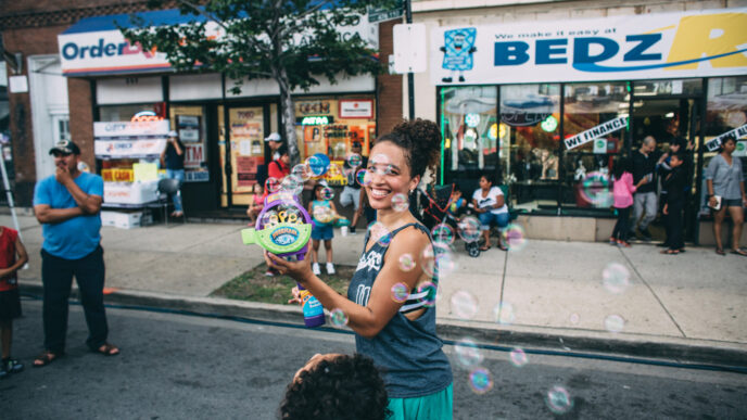 Woman smiling holding a bubble maker on the sidewalk.