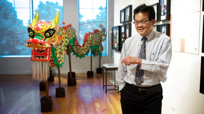 Dr. Kim Tee in front of a dragon puppet at the Chinese-American Museum of Chicago|Dr. Kim Tee stands smiling in a gallery at the Chinese American Museum of Chicago.