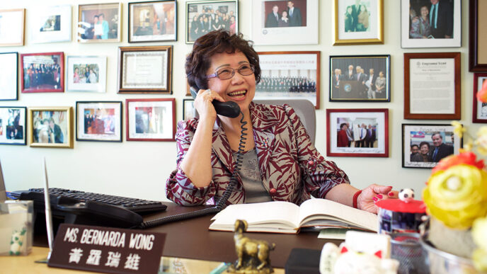 Bernie Wong talks on the phone in her office at the Chinese American Service League|Bernie Wong leads children through a playground game|.