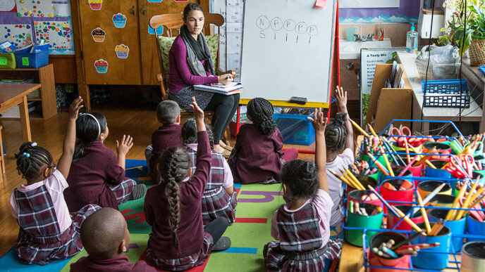 An elementary school class sits on the floor around a teacher in a rocking chair.