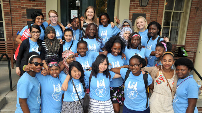 Blair Brettschneider stands on a staircase with a group of students from GirlForward.