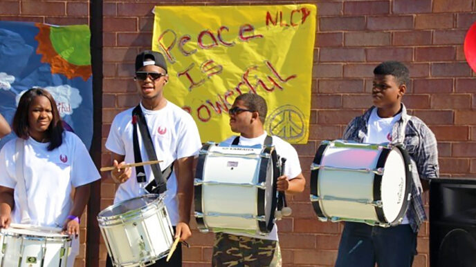 NLCP students stand with marching drums in front of a poster reading 'Peace is Powerful'.