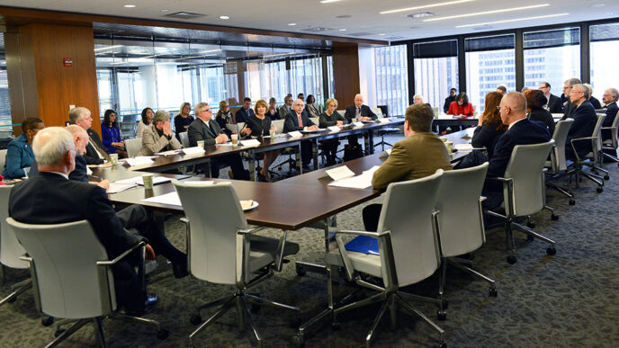 Representatives of 20 colleges meet around a table.