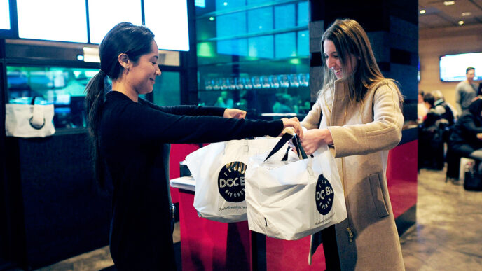 Culinary Care founder Courtney White picks up meals ready to deliver from Doc B's restaurant|Courtney White sits on the hospital bed and talks with a patient during a meal delivery.