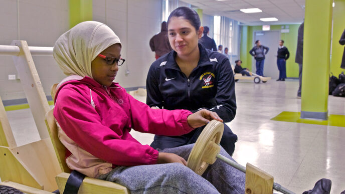 A student from Phoenix Academy helps a young girl steer a wooden boxcar.