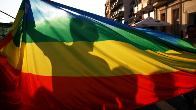 A man in silhouette behind a rainbow Pride flag