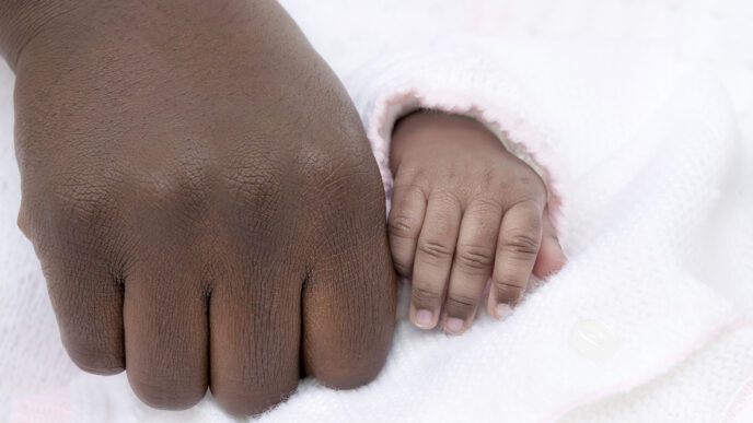 A man's hand rests besides that of a baby.