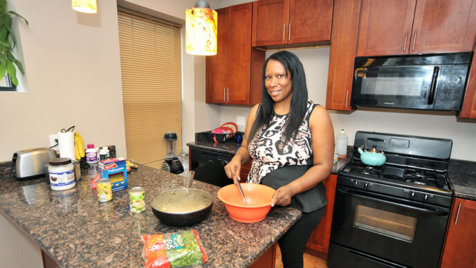Akeeta Murphy stands at her kitchen counter stirring food in a bowl while preparing a meal|Murphy stands by a window looking out.