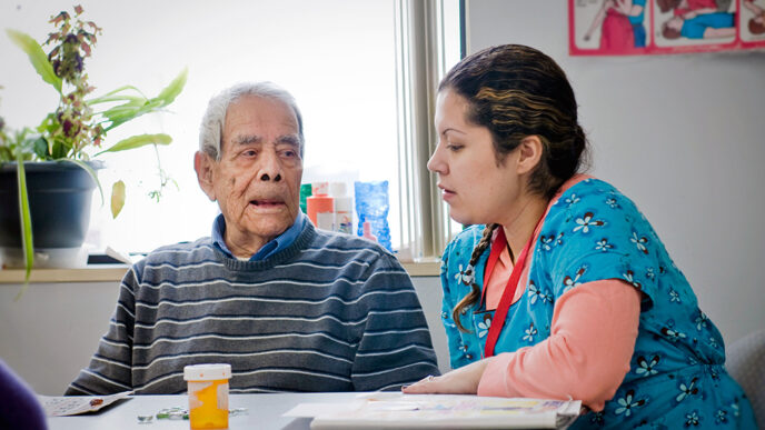 A senior man sits and talks with a health care worker at Casa Central|Map of Illinois color-coded to show the decline in state funding dollars to human services by county.