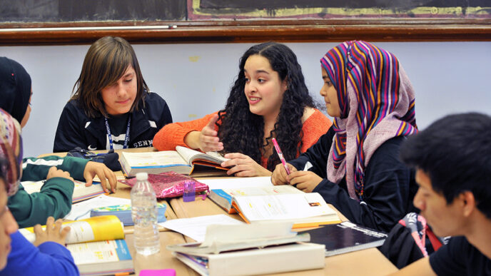 A teacher kneels beside a table of high school students.