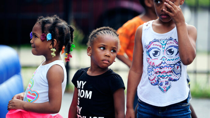 Three girls standing and waiting for their turn to perform|A crowd gathered in a parking lot.