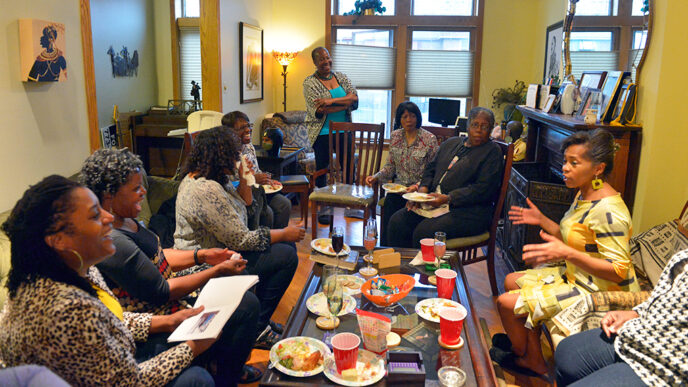 A group of women sit in a living room holding books and having a conversation|A team of people creates a large mosaic on an exterior wall.