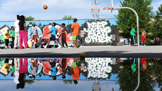A group plays basketball in front of a mural reading Keep Loving Each Other.