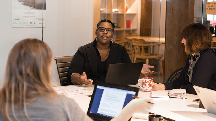 Brandies Meva'a and colleagues meeting in a conference room|Sandee Kastrul.