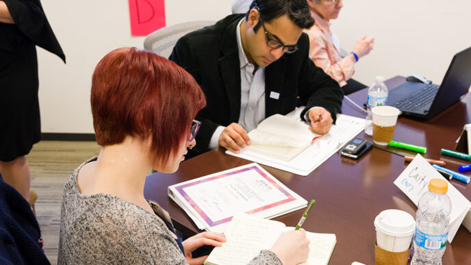 Two people sit at a table and take notes|Two women seated at a table laughing.