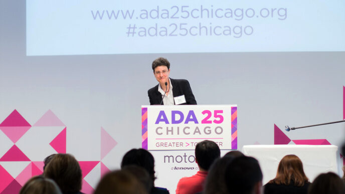 Emily Harris standing on stage at a podium with a sign that reads ADA 25 Chicago - Greater Together|.