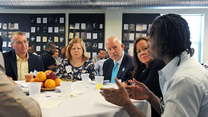 A group of people seated at a table; one man speaks and gestures with his hands