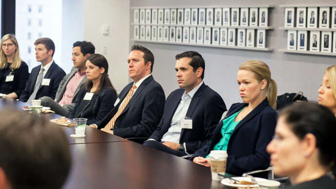 A row of people seated at a ing boardroom table listening intently|James Vender|Pam Berkowitz.