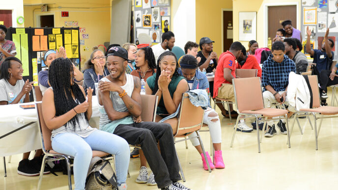 A large group of teenaged sitting in chairs in a basement room.