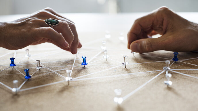 Two hands place pushpins into a board