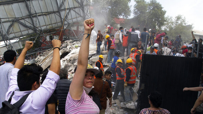 Rescue workers in safety vests and hard hats climb through the rubble of buildings.