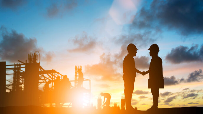 A construction site at sunrise. Two people shaking hands are pictured in silhouette.