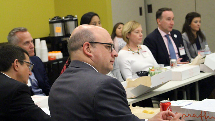 A group of men and women sit around a large table with boxed lunches.