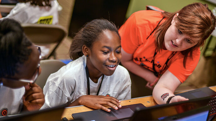 A smiling teenage girl works at a laptop.