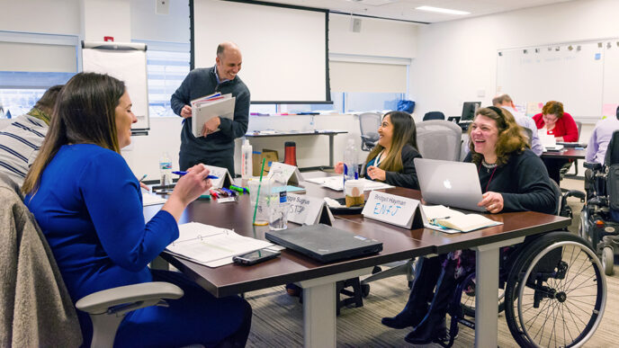 Four people seated in chars and wheelchairs around a table in a conference room.