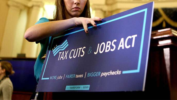 A young staffer affixes a sign reading Tax Cuts and Jobs Act to a podium.