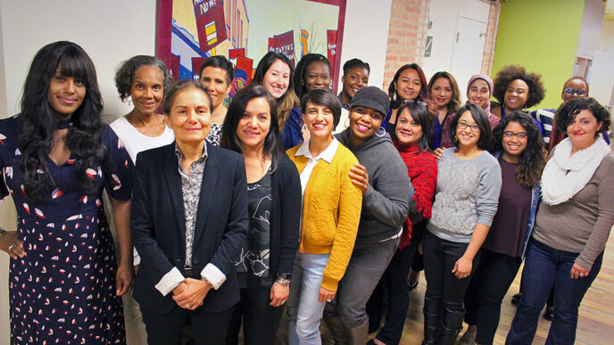 Nineteen women standing in a group indoors.