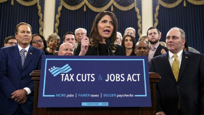 Rep. Kristi Noem of South Dakota stands at a podium holding a sign reading Tax Cuts and Jobs Act.